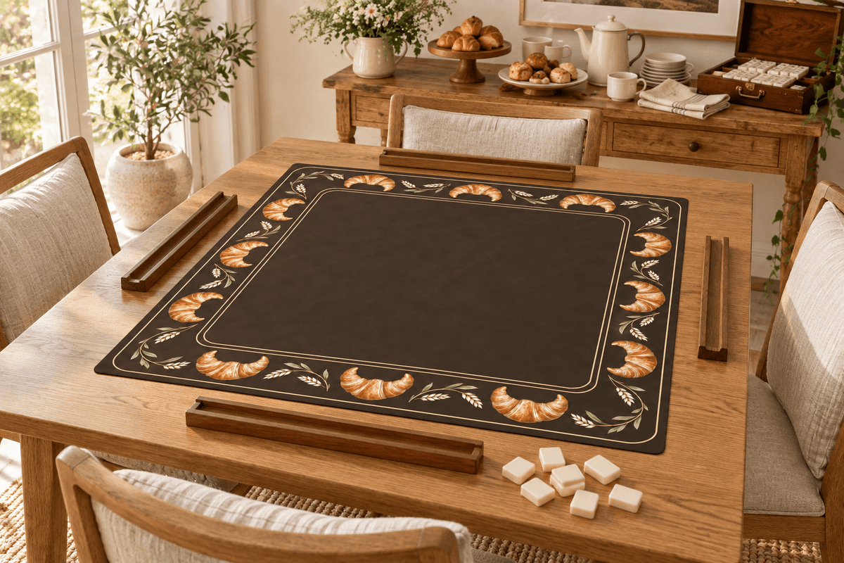 CROISSANT SOCIETY mahjong mat on an oak table with empty wooden racks and face-down tiles, beside a pastry and coffee station before play.